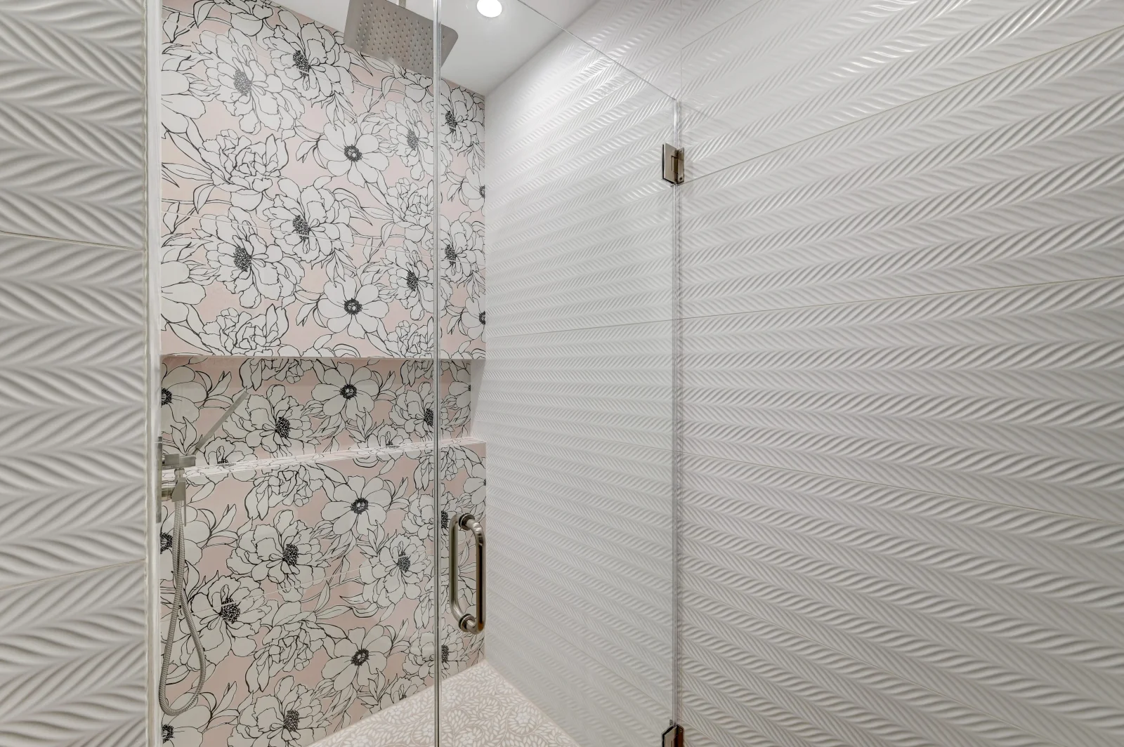 Ceramic tile shower with herringbone pattern walls and floral accent tiles, frameless glass enclosure