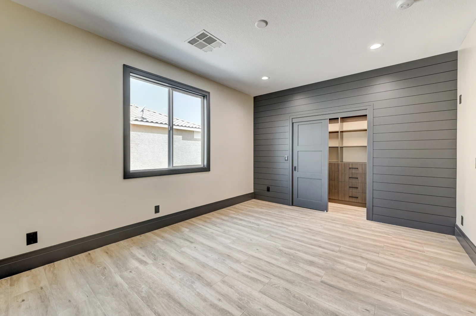 Bedroom with gray shiplap wall, vinyl plank flooring, built-in shelving, and black-framed window
