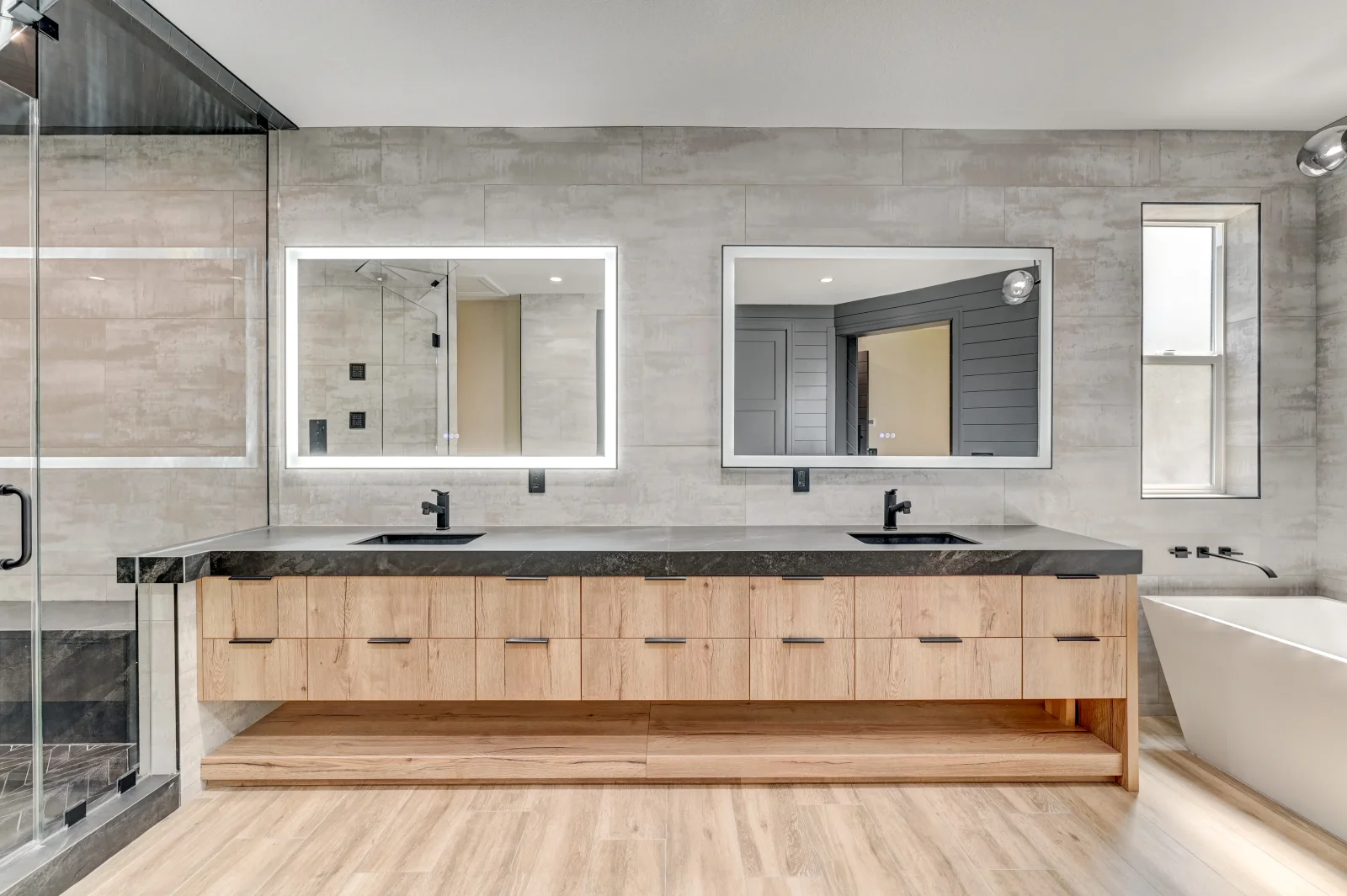 Master bathroom with double vanity, gray tile walls, quartz countertop, and frameless shower