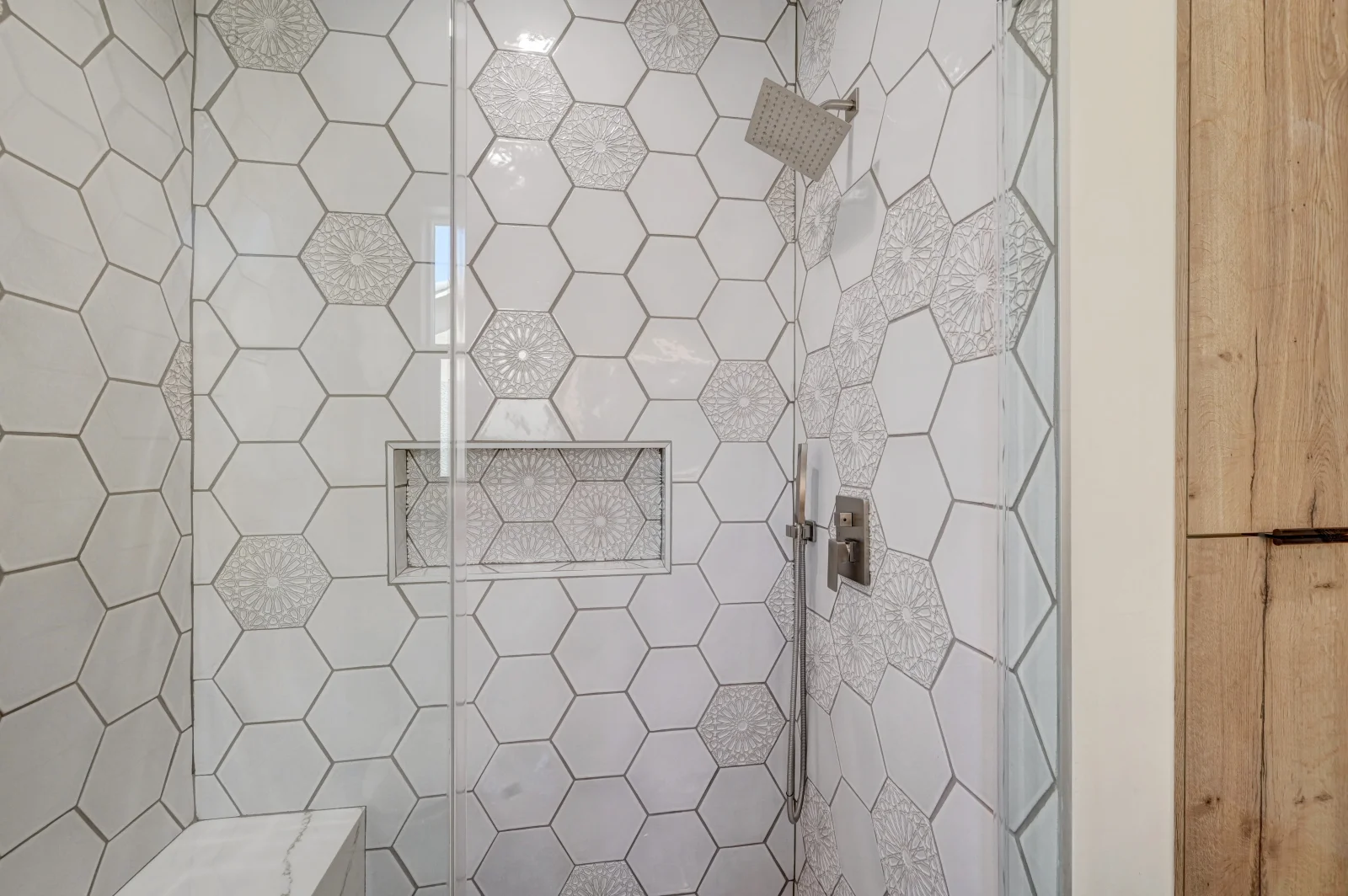 Hexagonal white porcelain tiles with patterned accents in walk-in shower with frameless glass door
