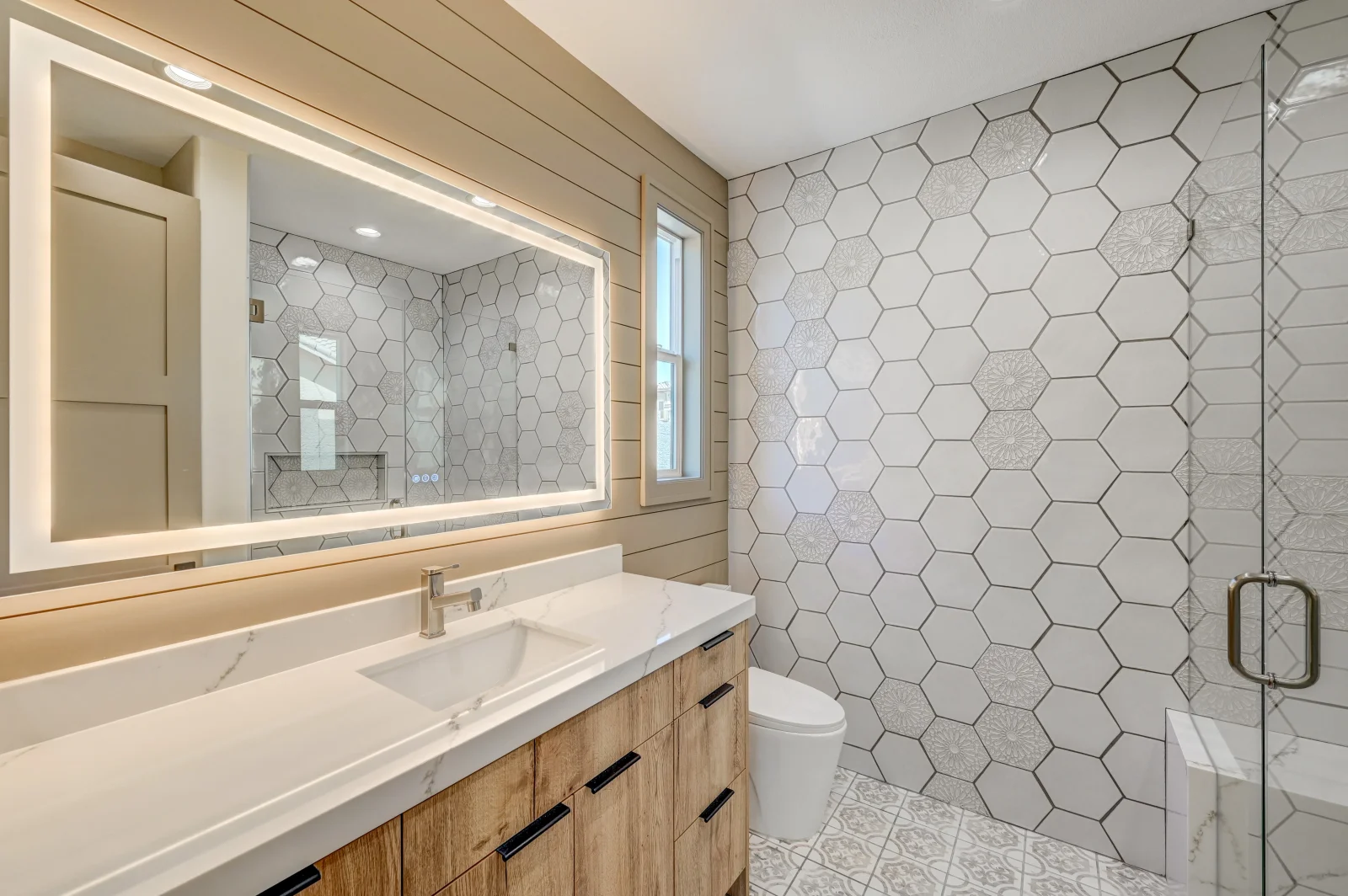 Modern bathroom with hexagonal marble tile walls, marble vanity, and frameless glass shower