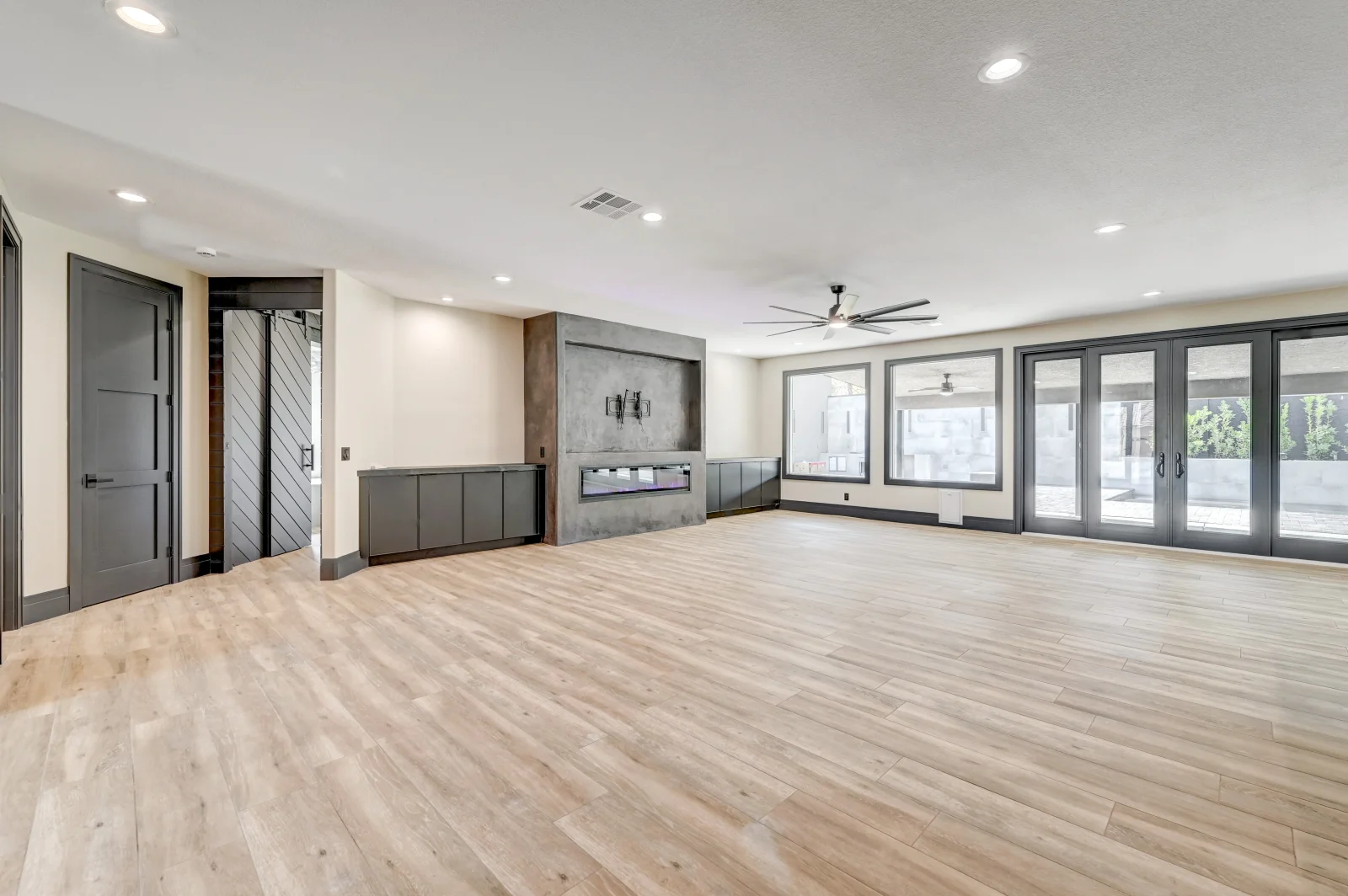 Open-concept room with light wood flooring, built-in cabinetry, concrete feature wall, and multi-panel glass doors