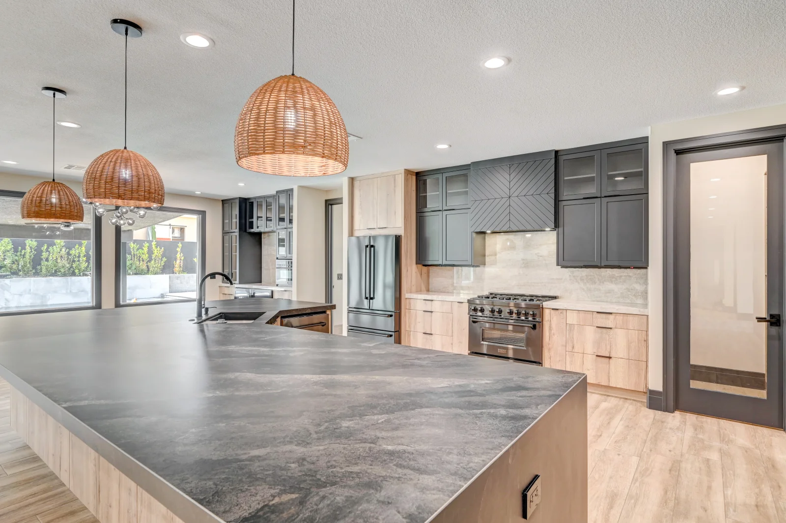Modern kitchen with concrete countertops, mixed wood and gray cabinetry, stainless steel range, and woven pendant lights