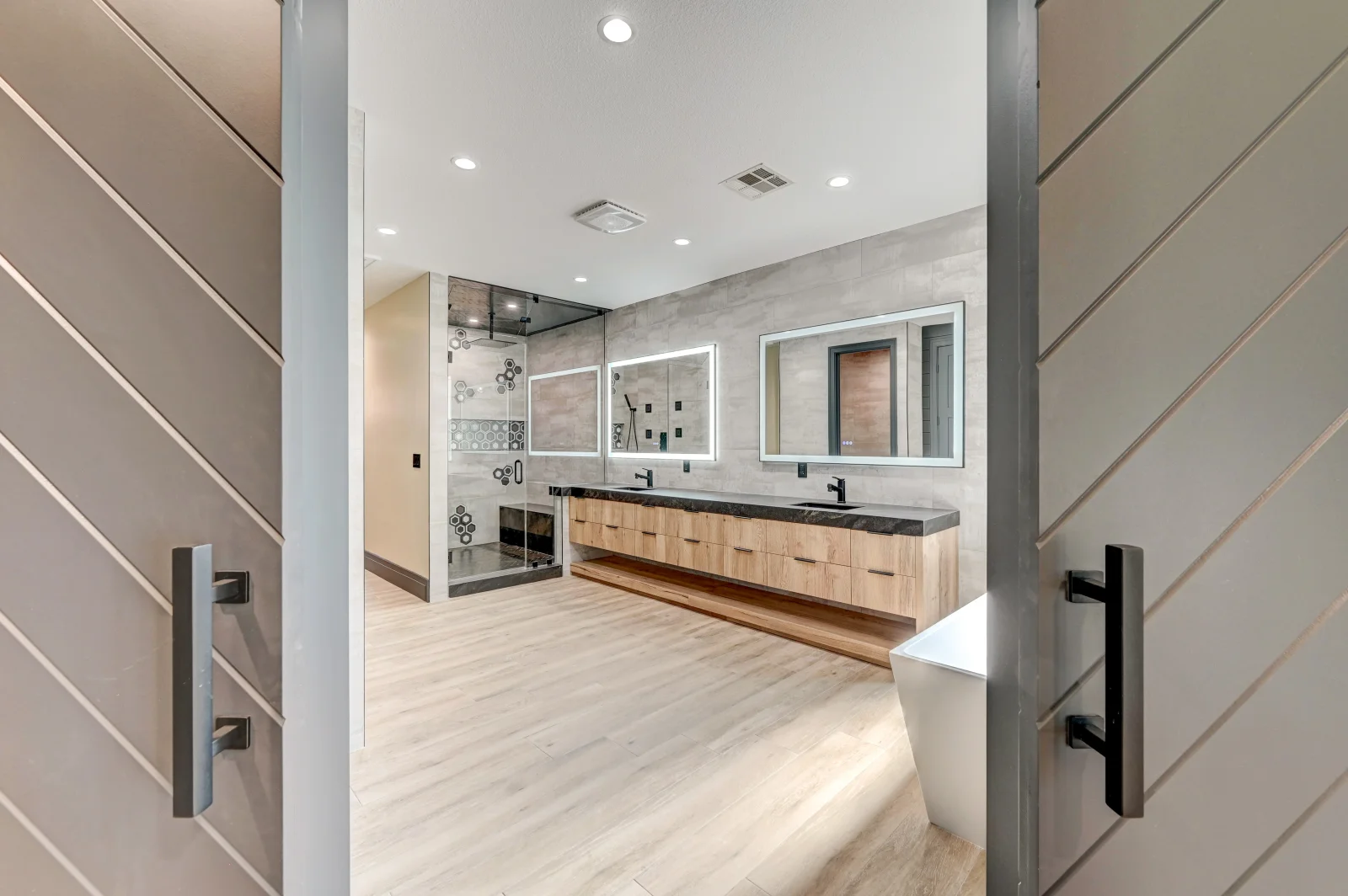 Master bathroom with wood vanity, dual sinks, frameless shower, and luxury vinyl flooring